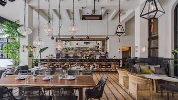 A restaurant with a bar area, wooden tables, wicker chairs, hanging lights, and a tiled floor.