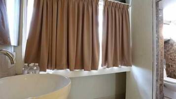 A bathroom with a sink, a window with curtains, and a toilet.