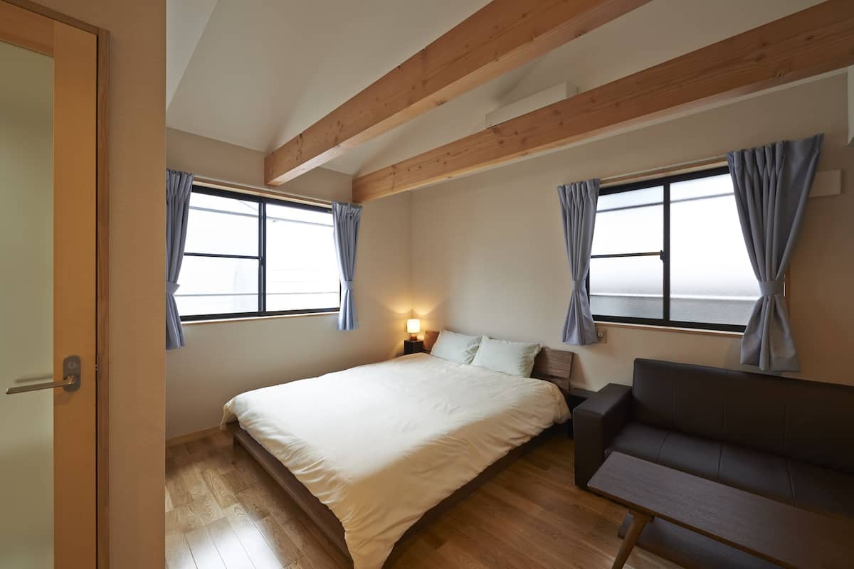 A bedroom with a bed, a sofa, a nightstand, and two windows with curtains.