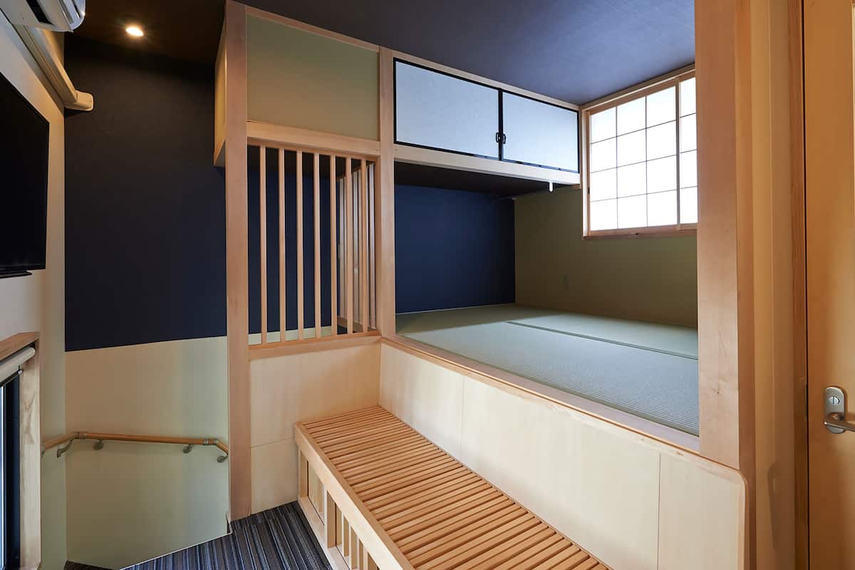 A room with a bunk bed, a small bench, a window, and a door.