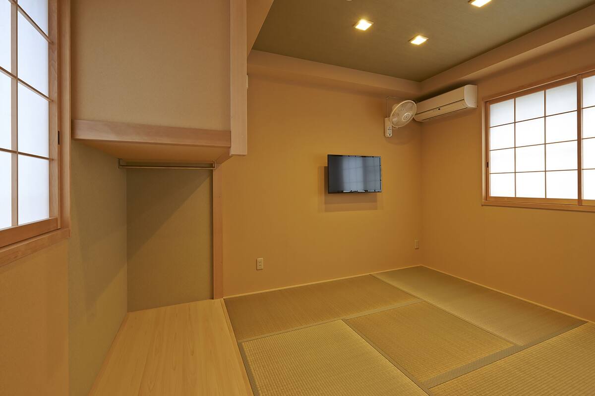 A room with tatami flooring, a mounted air conditioner, and a television on the wall.