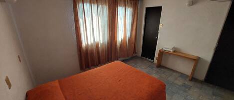 A room with a bed, a desk, a chair, a door, and a window with curtains.