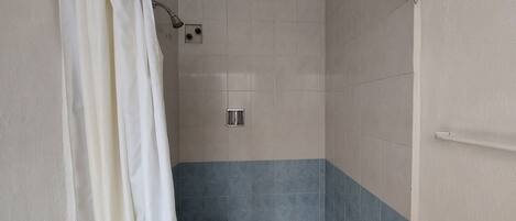 A shower area with a white curtain, tiled walls, and a metal showerhead.