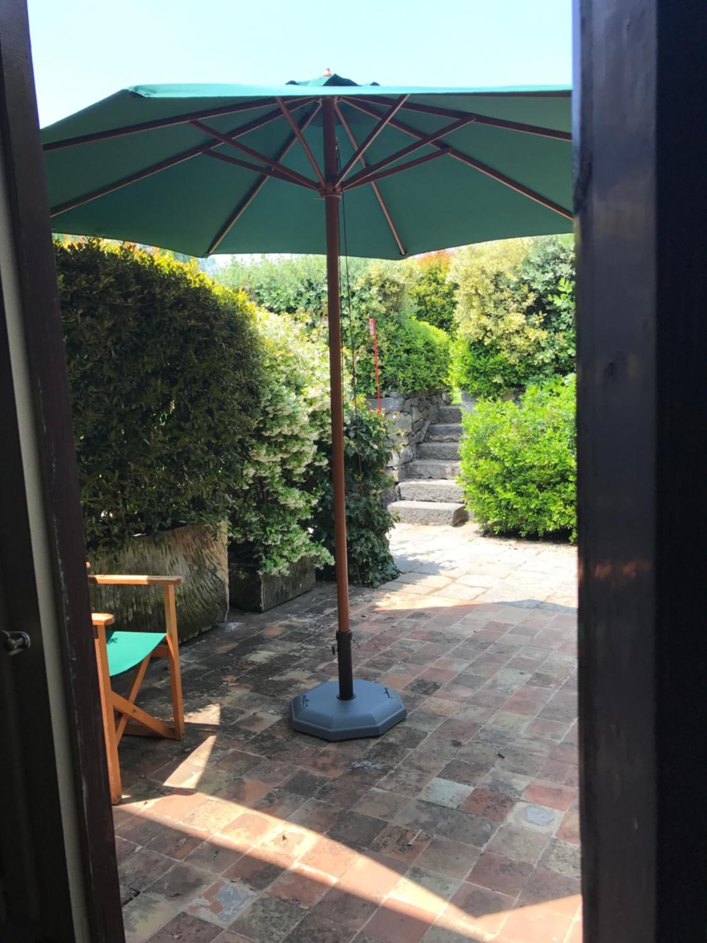 A patio area with a green umbrella, a wooden chair, and a stone wall.