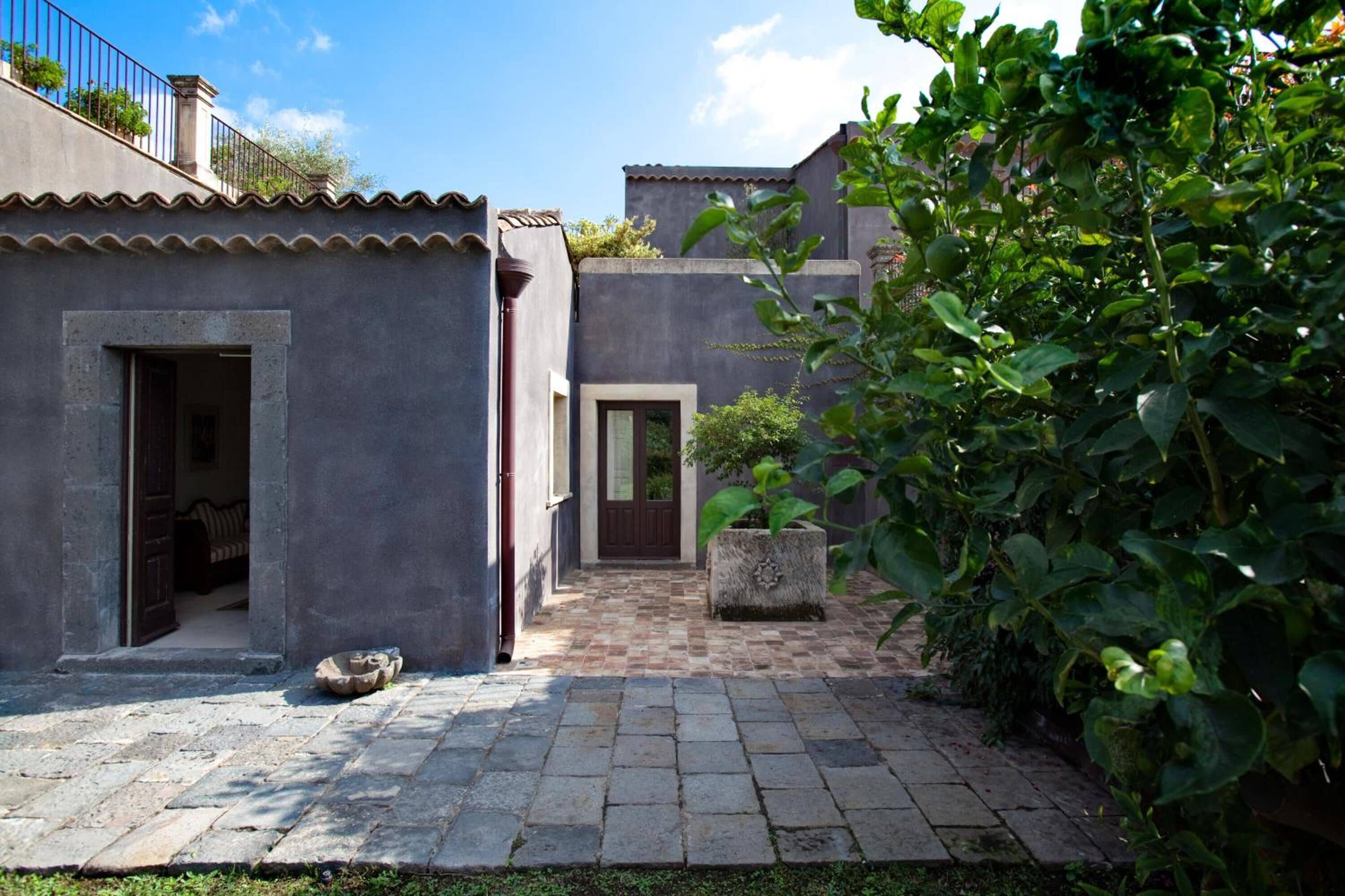 A courtyard with stone paving, two buildings with doors, and a potted plant.