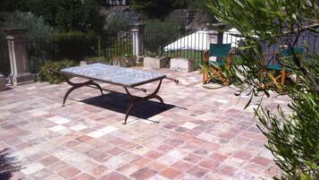 En terrasse med et metalbord og stole, omgivet af stenfliser og grønne planter.