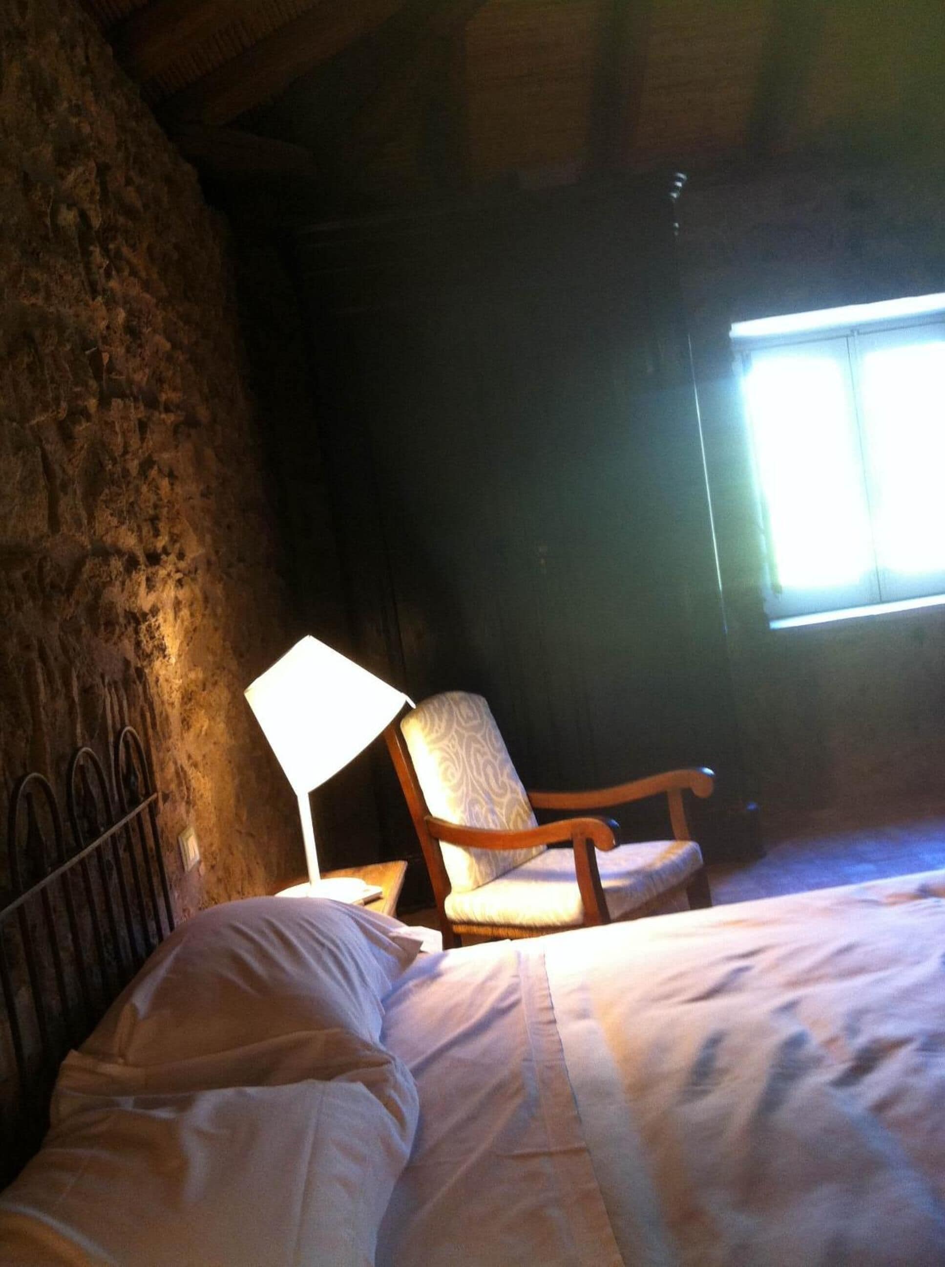 Une chambre rustique avec un lit, une chaise et une lampe.