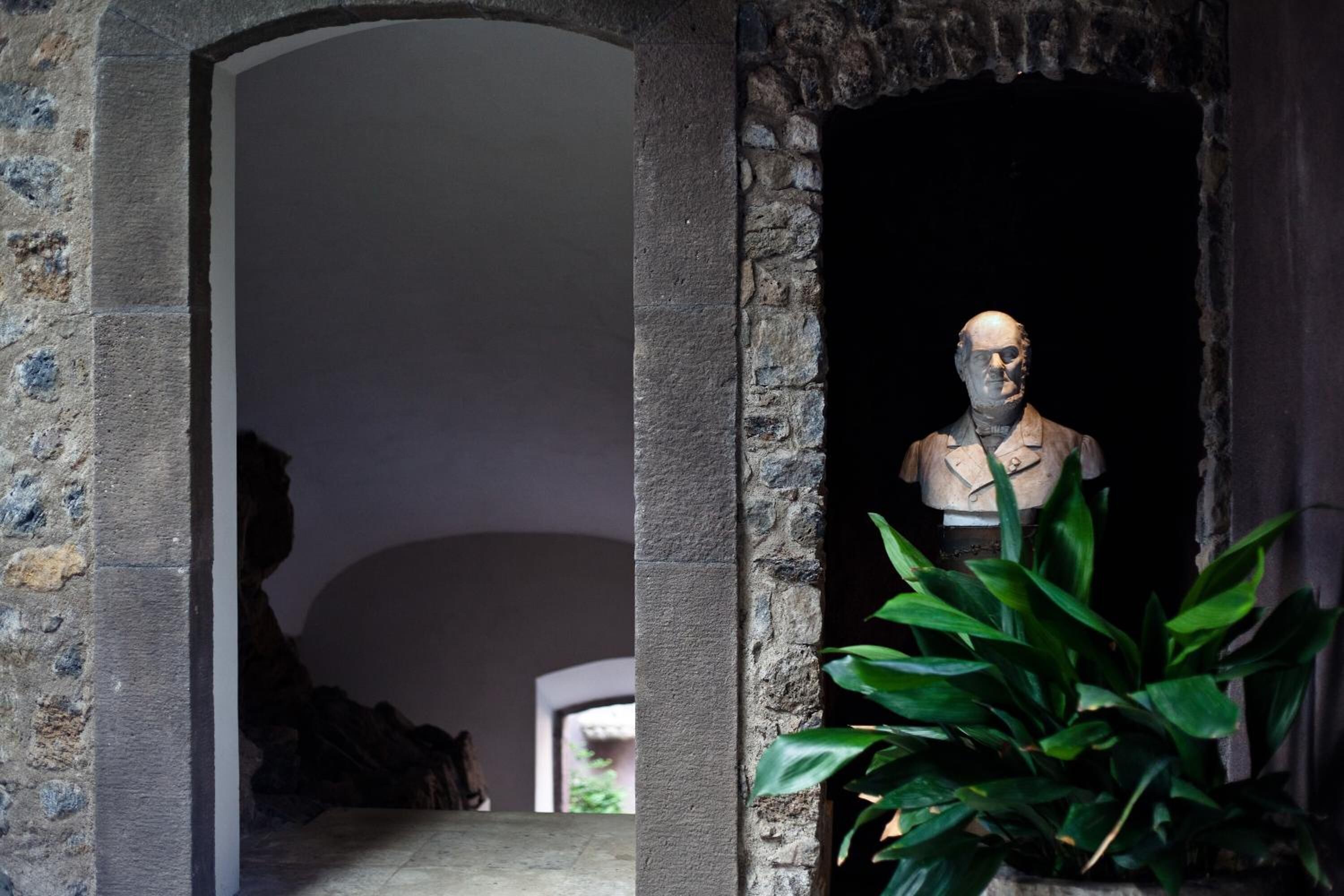 A statue in a stone archway with a potted plant in the foreground.