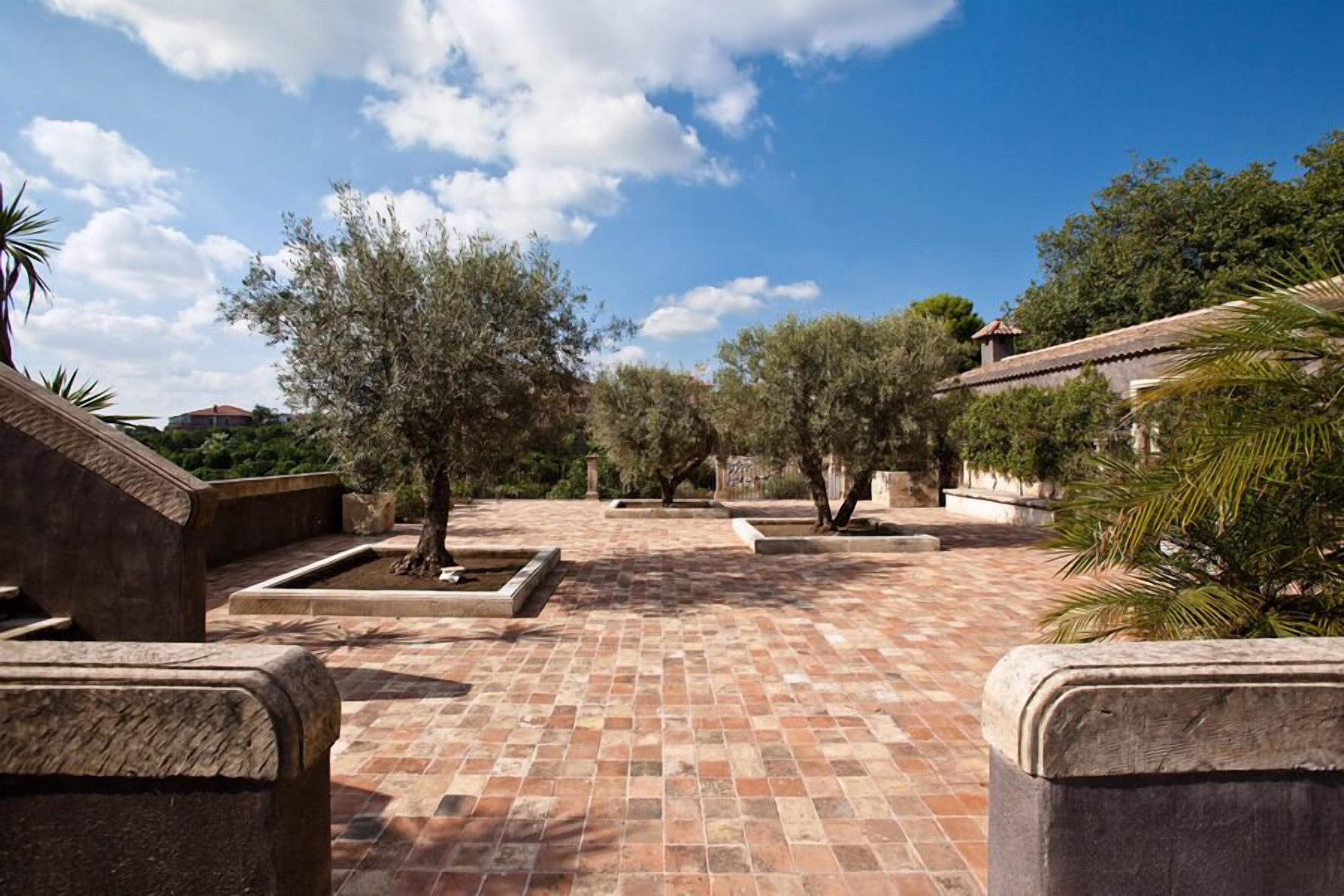 A courtyard with tiled flooring, stone planters, and trees.