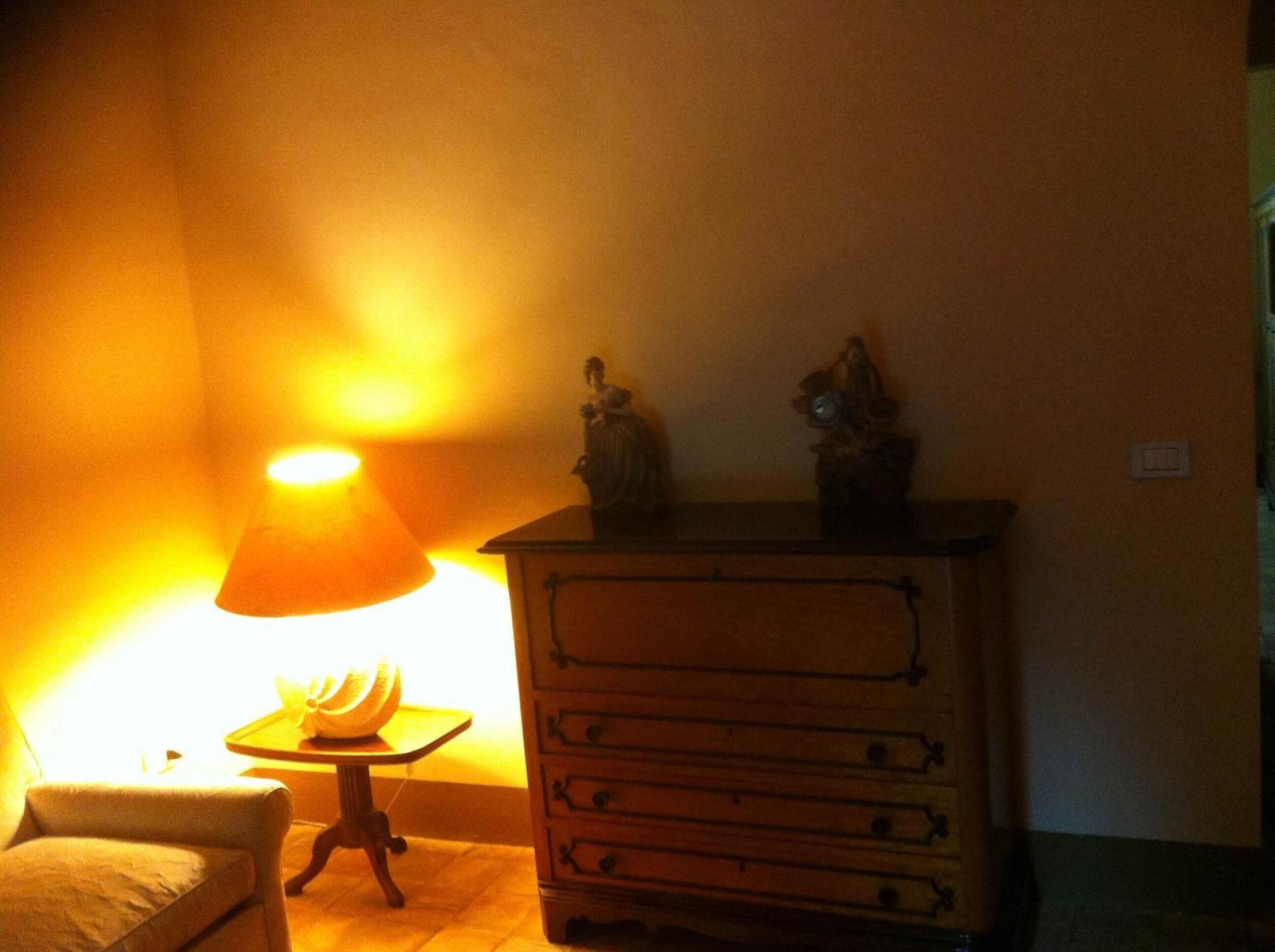 A room with a lamp casting a warm glow, a small table with a decorative item, and a wooden dresser with drawers.
