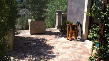 Eine Terrasse mit Steinboden, einem Holzstuhl und einem Steinpflanzgefäß.