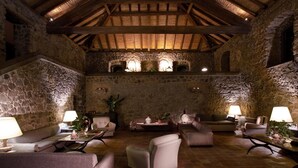 Un interior rústico con paredes de piedra, vigas de madera y un rincón acogedor con sofás y mesas.