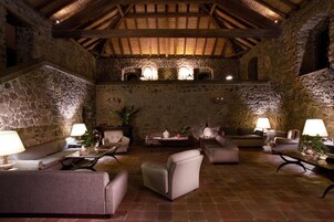 Un interior rústico con paredes de piedra, vigas de madera y un rincón acogedor con sofás y mesas.