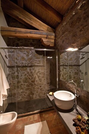 A bathroom with a stone wall, a glass shower enclosure, a white sink, and a wooden ceiling. - Casa la Carrubbazza (San Gregorio di Catania)