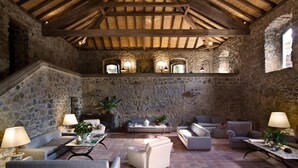 Un interior rústico de piedra con un alto techo de madera, paredes de piedra y zonas de estar amuebladas.