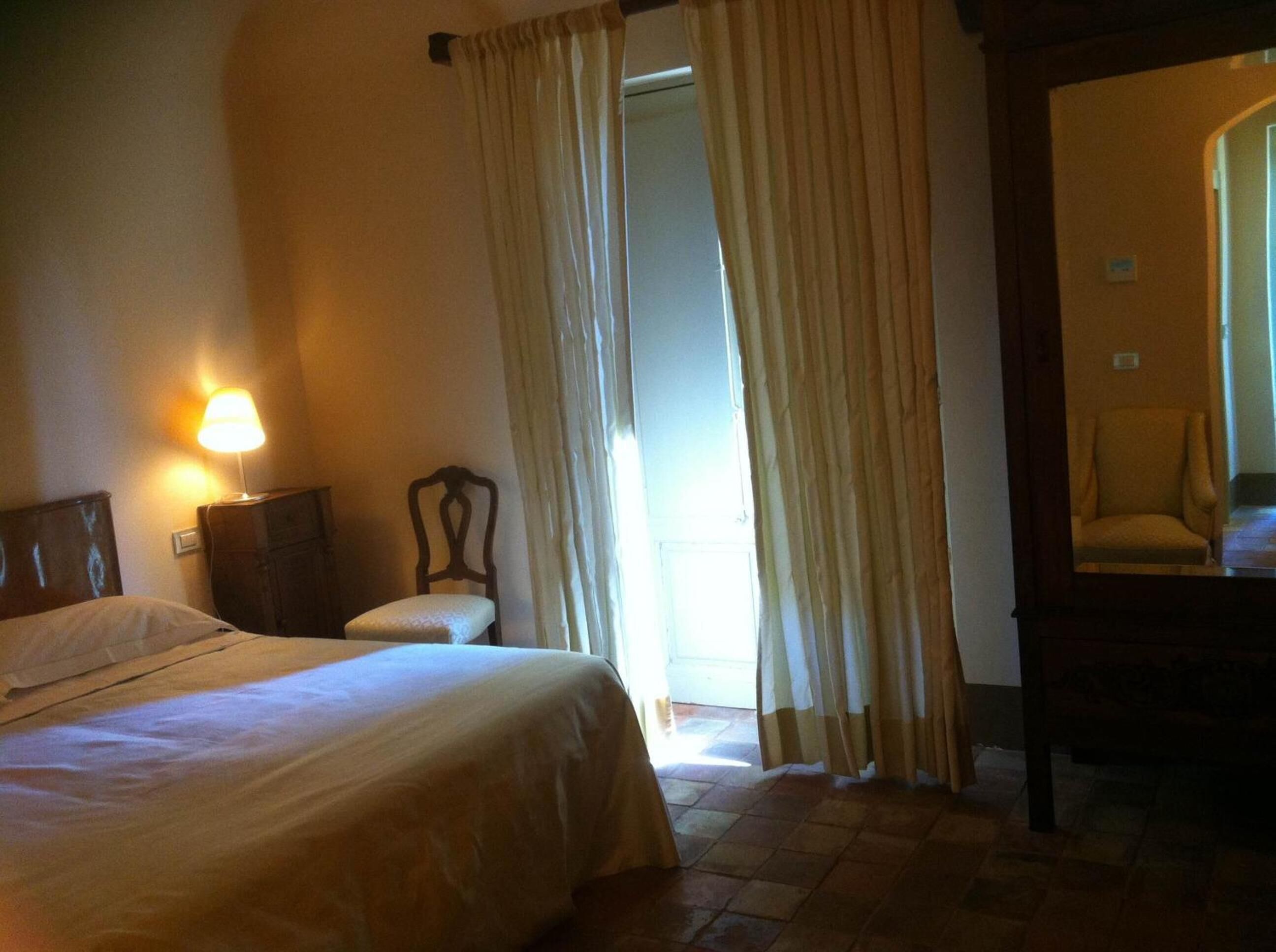 Una habitación de hotel con una cama, una mesita de noche, una silla y un espejo.