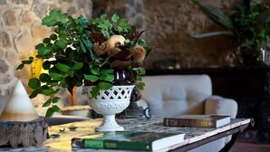 Un jarrón decorativo con follaje y flores secas sobre una mesa en una habitación con pared de piedra y un sofá.