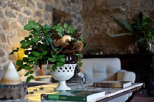 Un jarrón decorativo con follaje y flores secas sobre una mesa en una habitación con pared de piedra y un sofá.