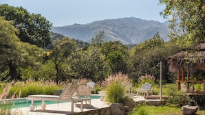 A pool area with lounge chairs, a thatched-roof structure, and a mountainous backdrop. - Las Dalias (Las Rosas)