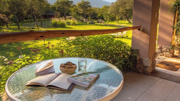 A round glass table with books and a bowl of fruit, set on a balcony overlooking a lush garden and distant mountains. - Las Dalias (Las Rosas)