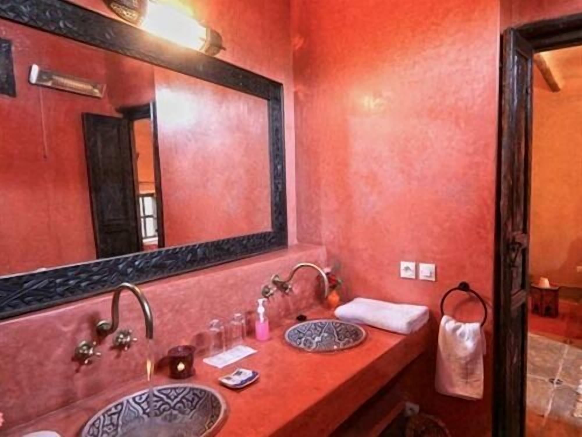 A bathroom with a red wall, a large mirror, two sinks, and a towel rack.