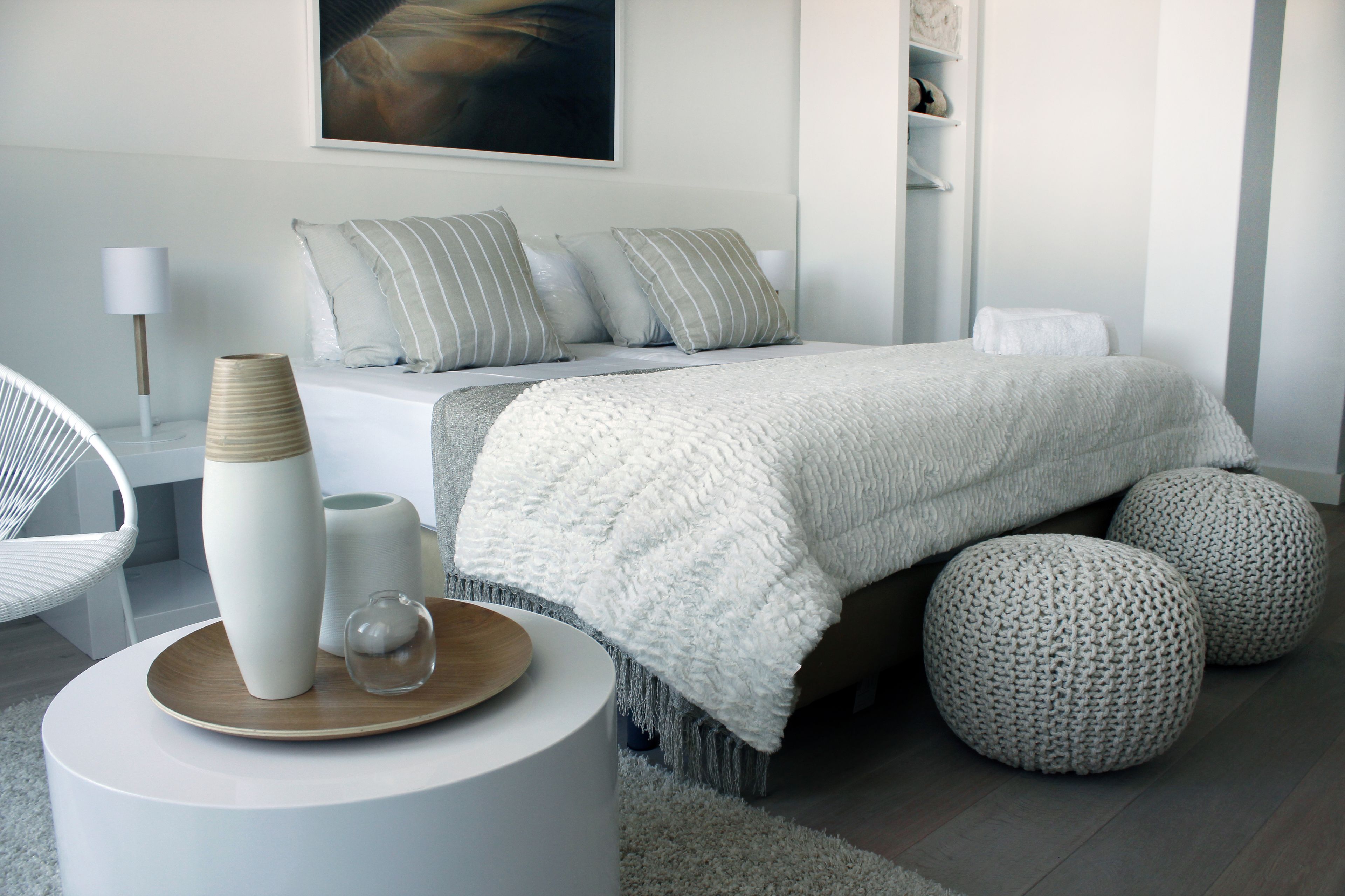 Quarto moderno com cama, mesas de cabeceira, uma cadeira e objetos decorativos.