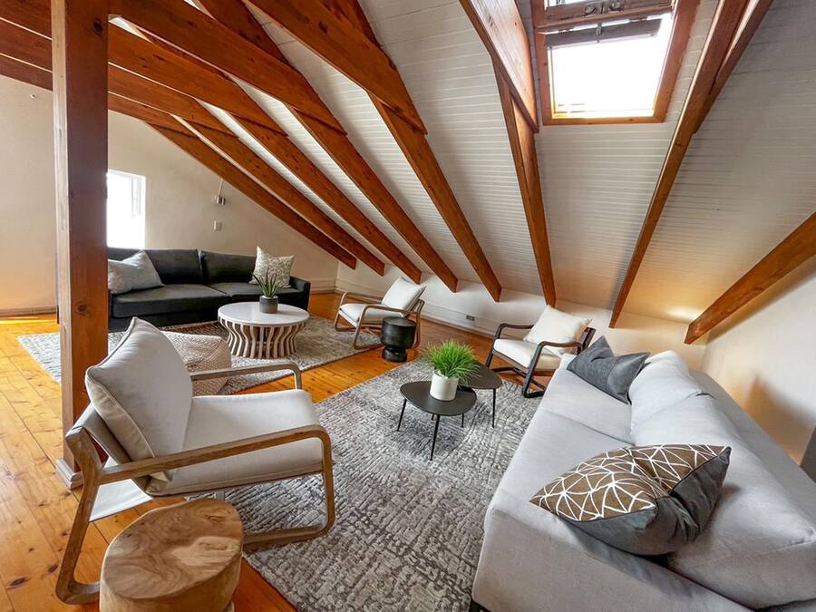 A spacious loft with high ceilings, exposed wooden beams, a cozy seating area with a sofa, chairs, and a coffee table, and a large skylight providing natural light.