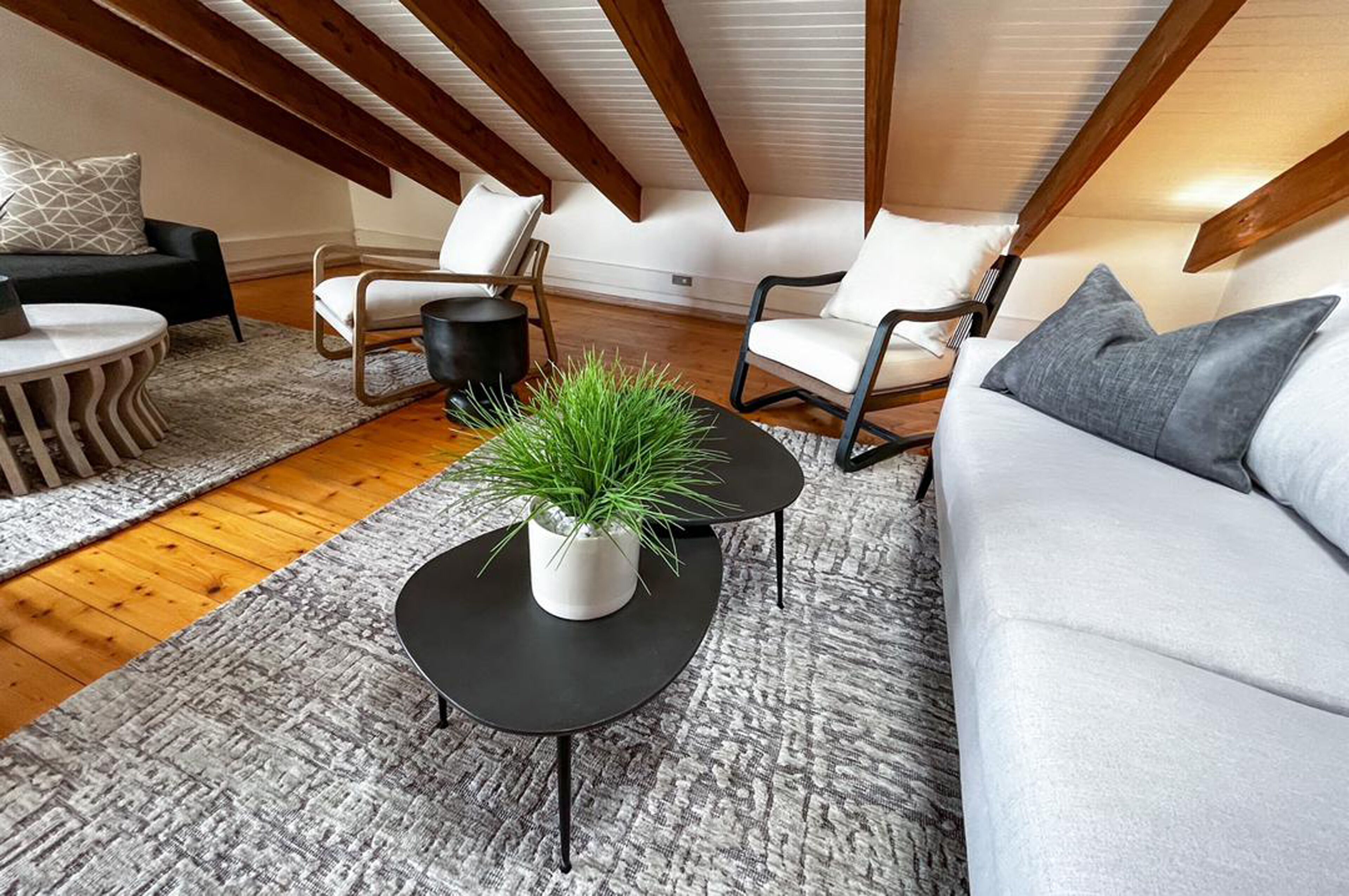 A modern loft-style living room with a high ceiling, exposed wooden beams, and a mix of contemporary and classic furniture.