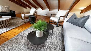 A modern loft-style living room with a high ceiling, exposed wooden beams, and a mix of contemporary and classic furniture.