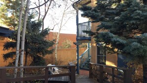 A wooden deck leading to a blue staircase with a railing, surrounded by trees and a building with a brown wall. - Guadalupe Inn (Santa Fe)