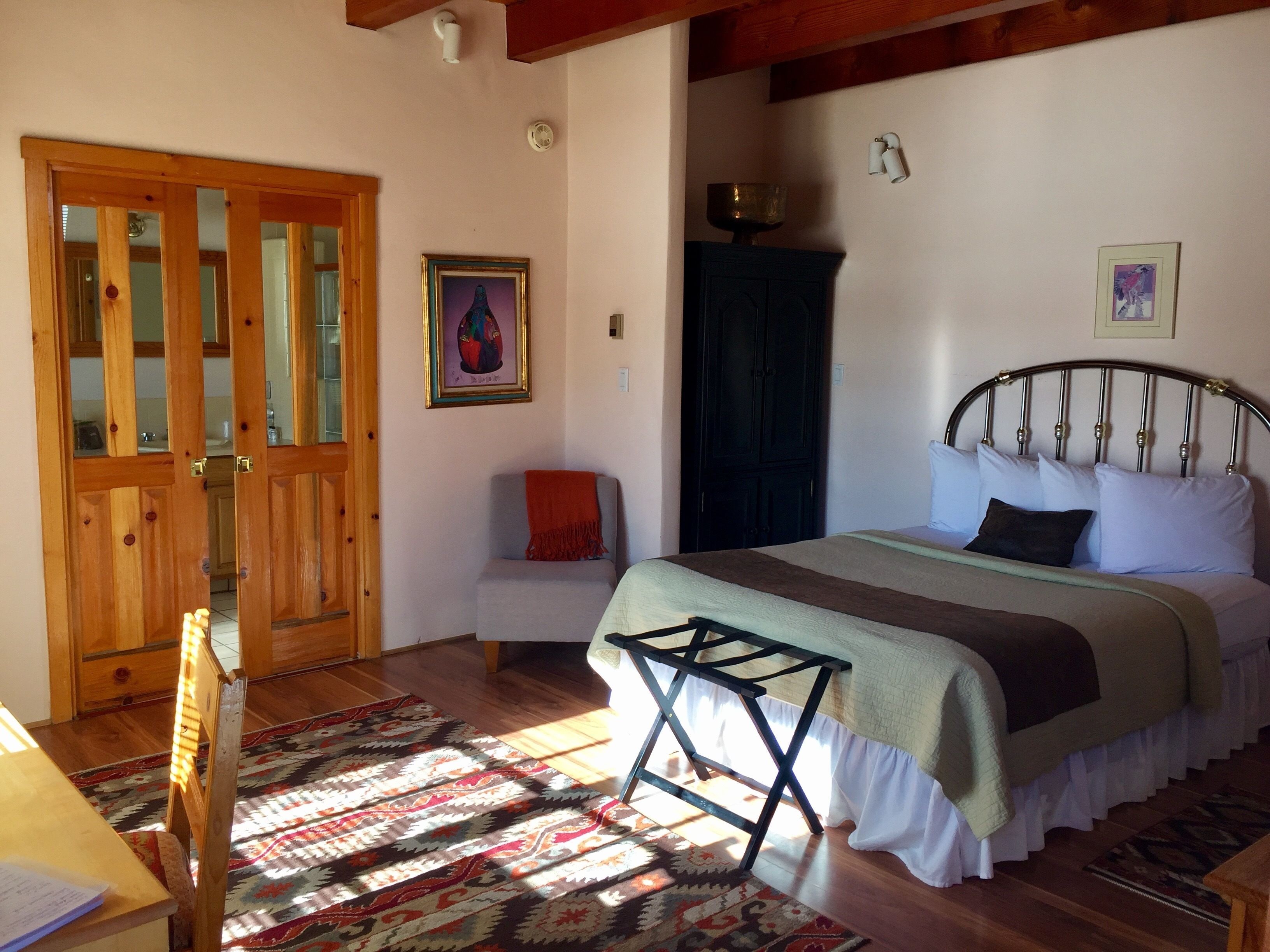 A bedroom with a bed, a chair, a wooden door, a painting, and a window.
