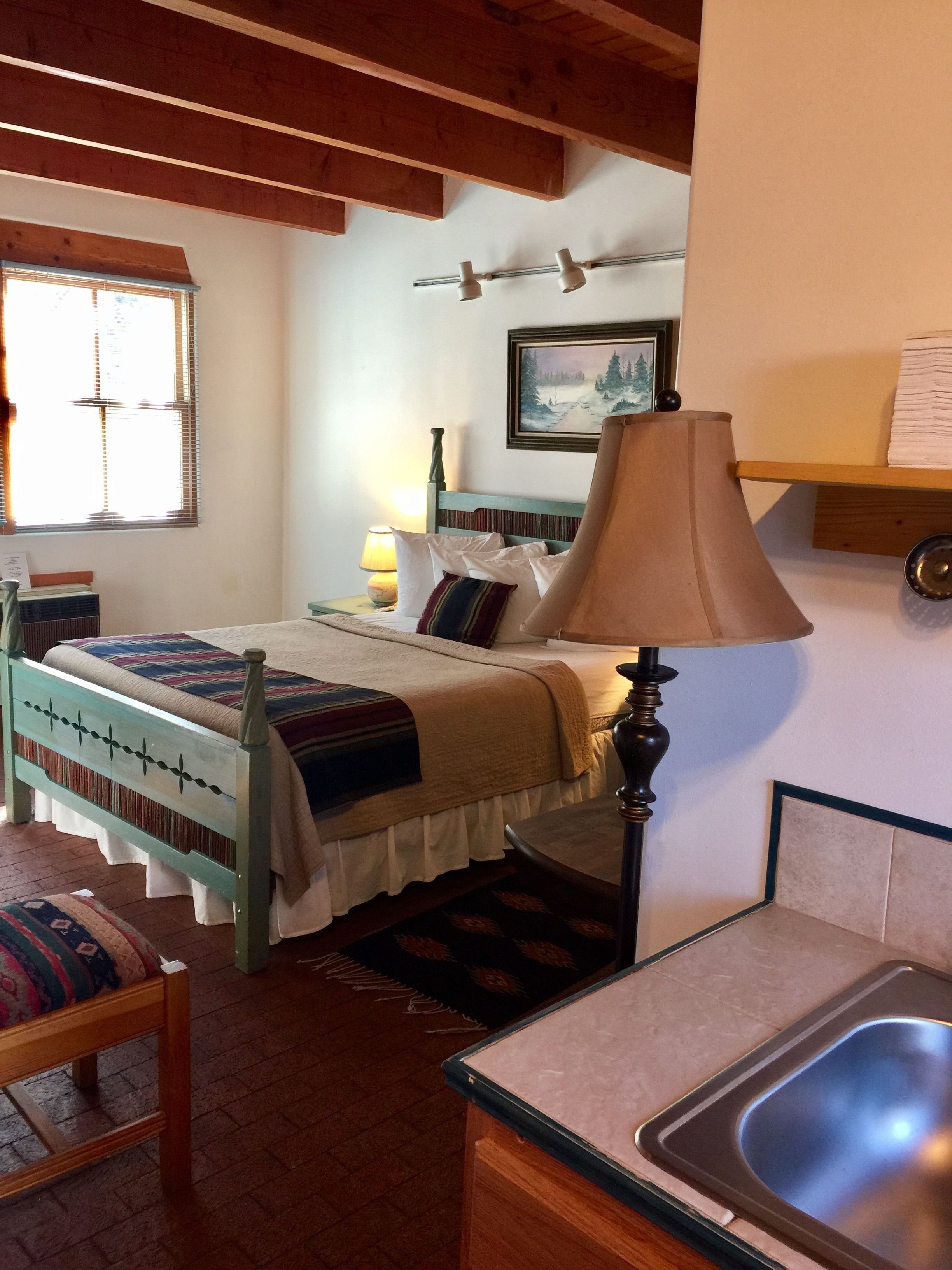 Un dormitorio acogedor con una cama de madera, una lámpara de noche, un cuadro en la pared y una ventana con persianas.