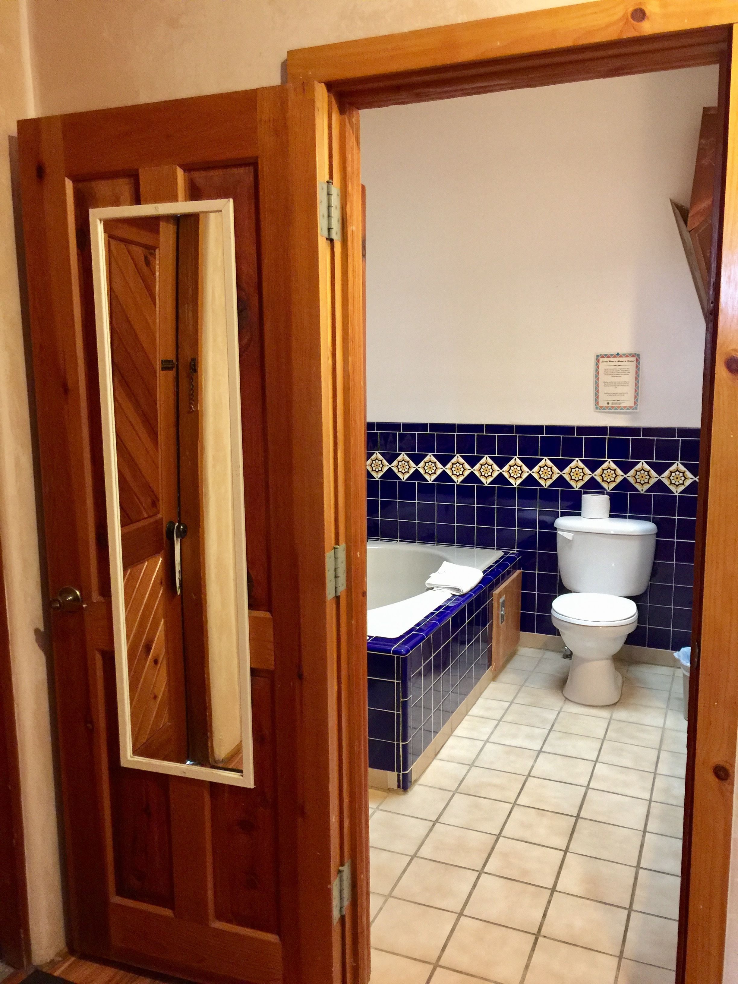A wooden door leading into a bathroom with a bathtub, toilet, and blue-tiled wall.