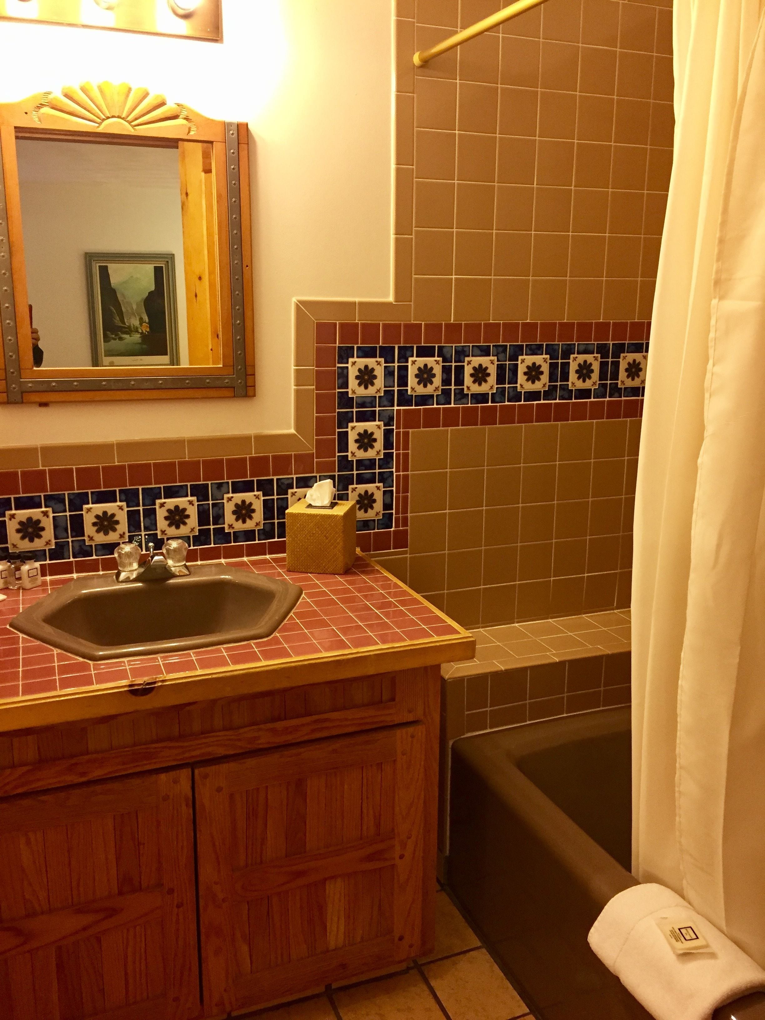 Een badkamer met een houten wastafelmeubel, een wastafel, een spiegel en een douchegedeelte.
