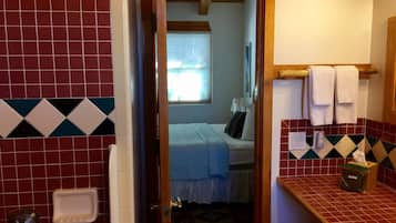 Une salle de bain avec des carreaux rouges et blancs, une porte en bois, un porte-serviettes avec des serviettes blanches et une petite poubelle.