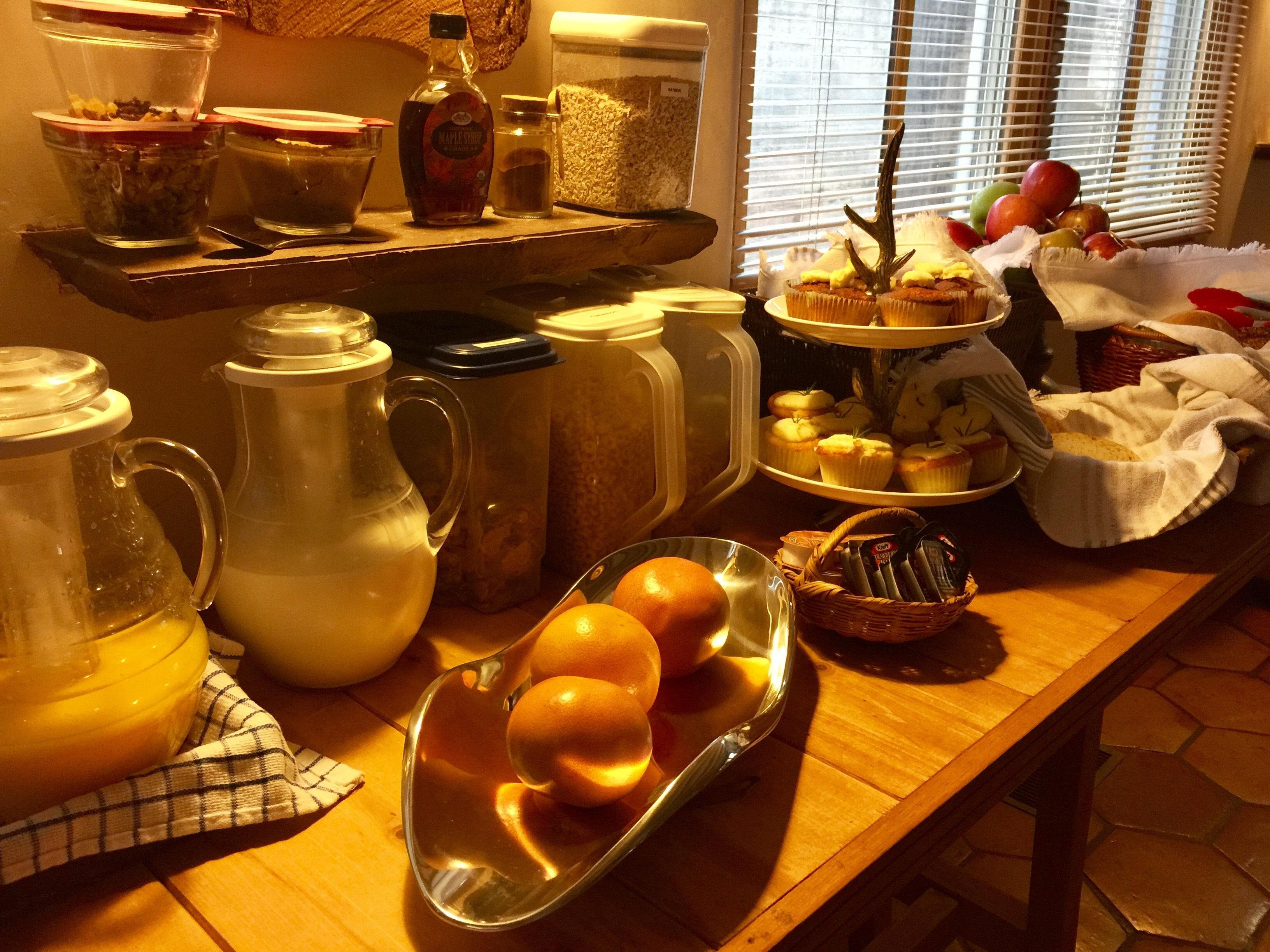 A kitchen counter with various food items, including a pitcher, a glass jar, and a plate of oranges.