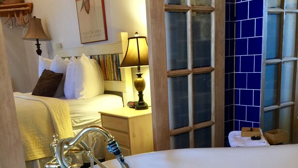 A bathroom with a freestanding bathtub, a wooden vanity with a mirror, and a blue-tiled wall. - Guadalupe Inn (Santa Fe)