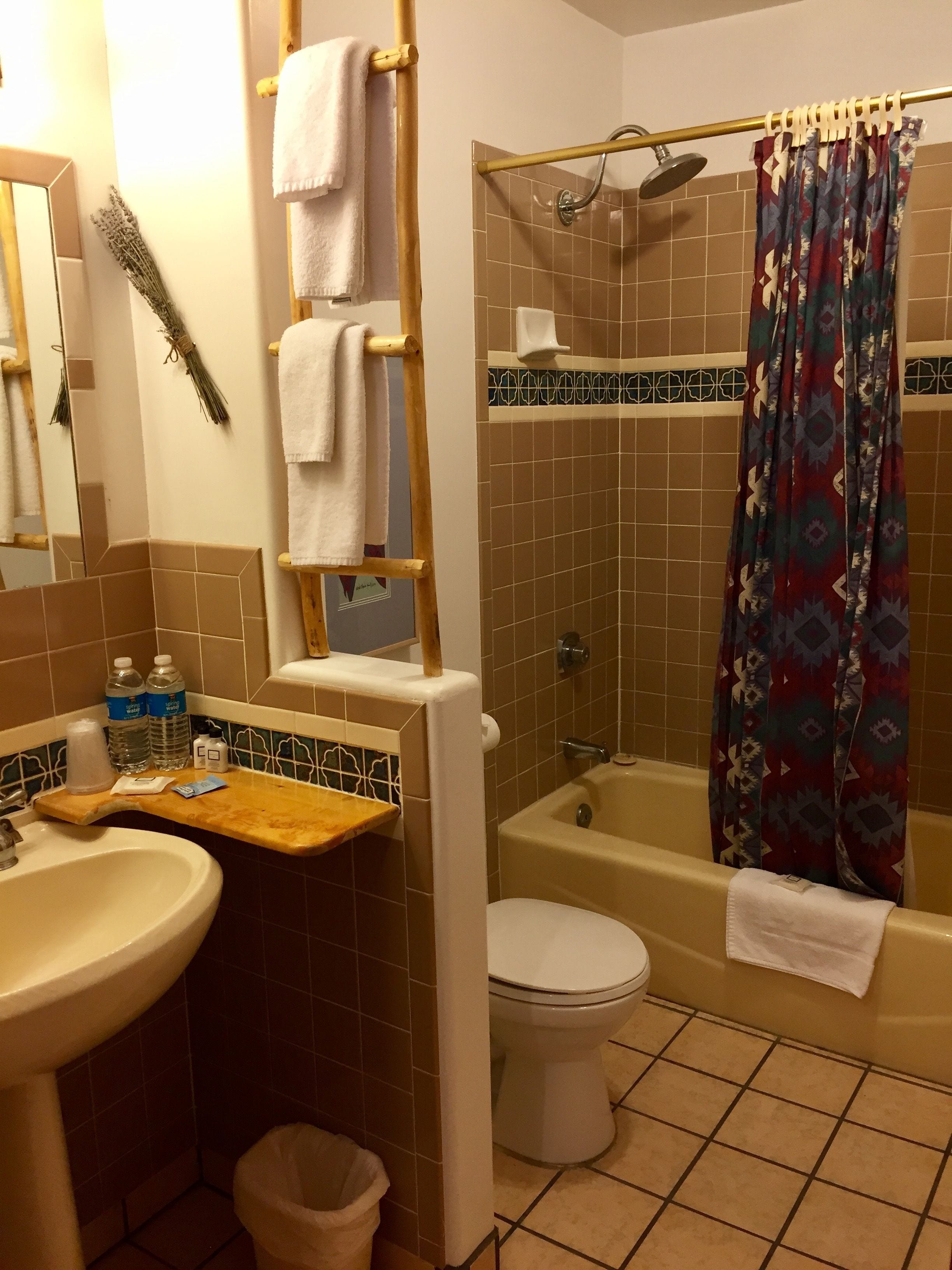 A bathroom with a sink, toilet, and bathtub. There are towels hanging on a rack, a shower curtain, and a mirror.