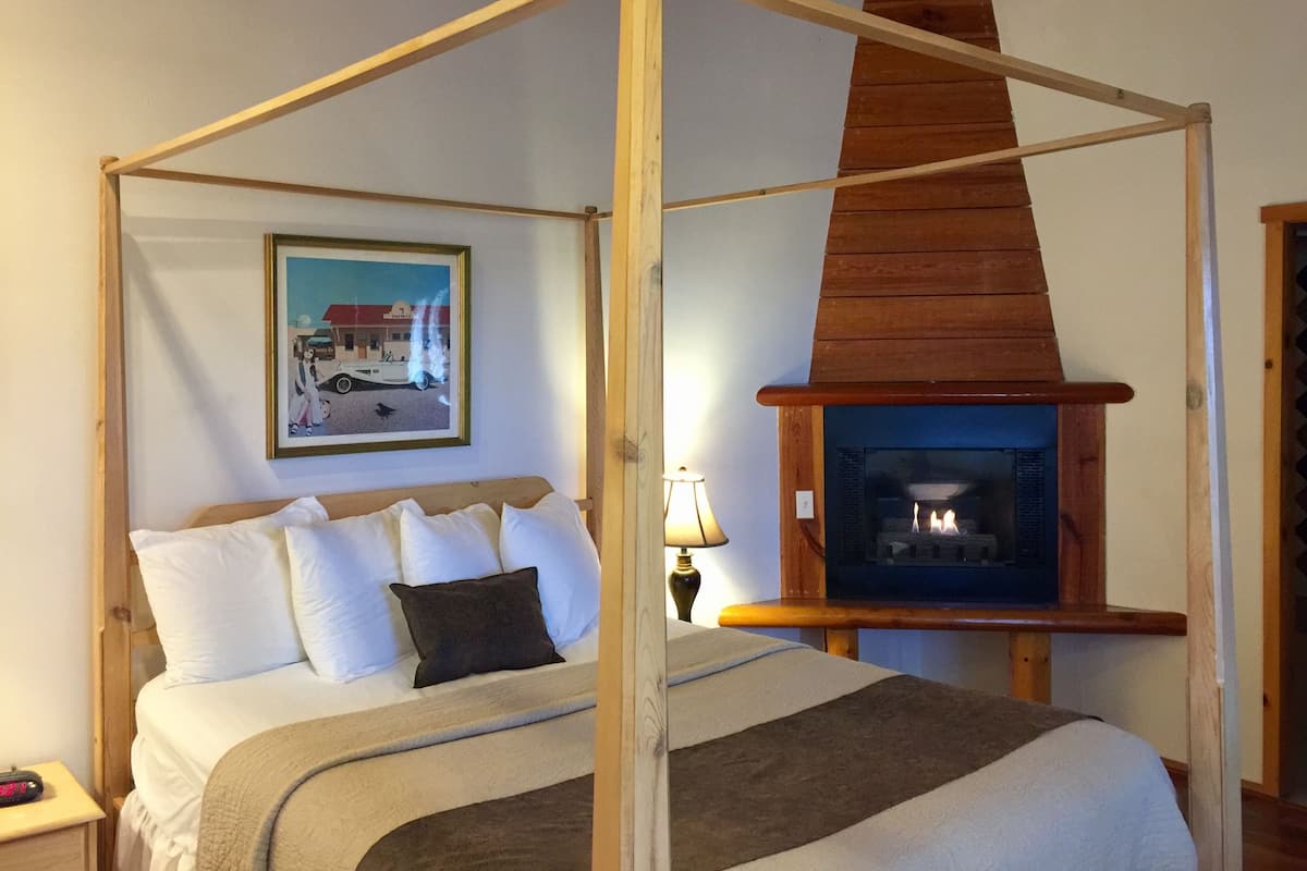 Quarto com cama de dossel, lareira e quadro na parede.