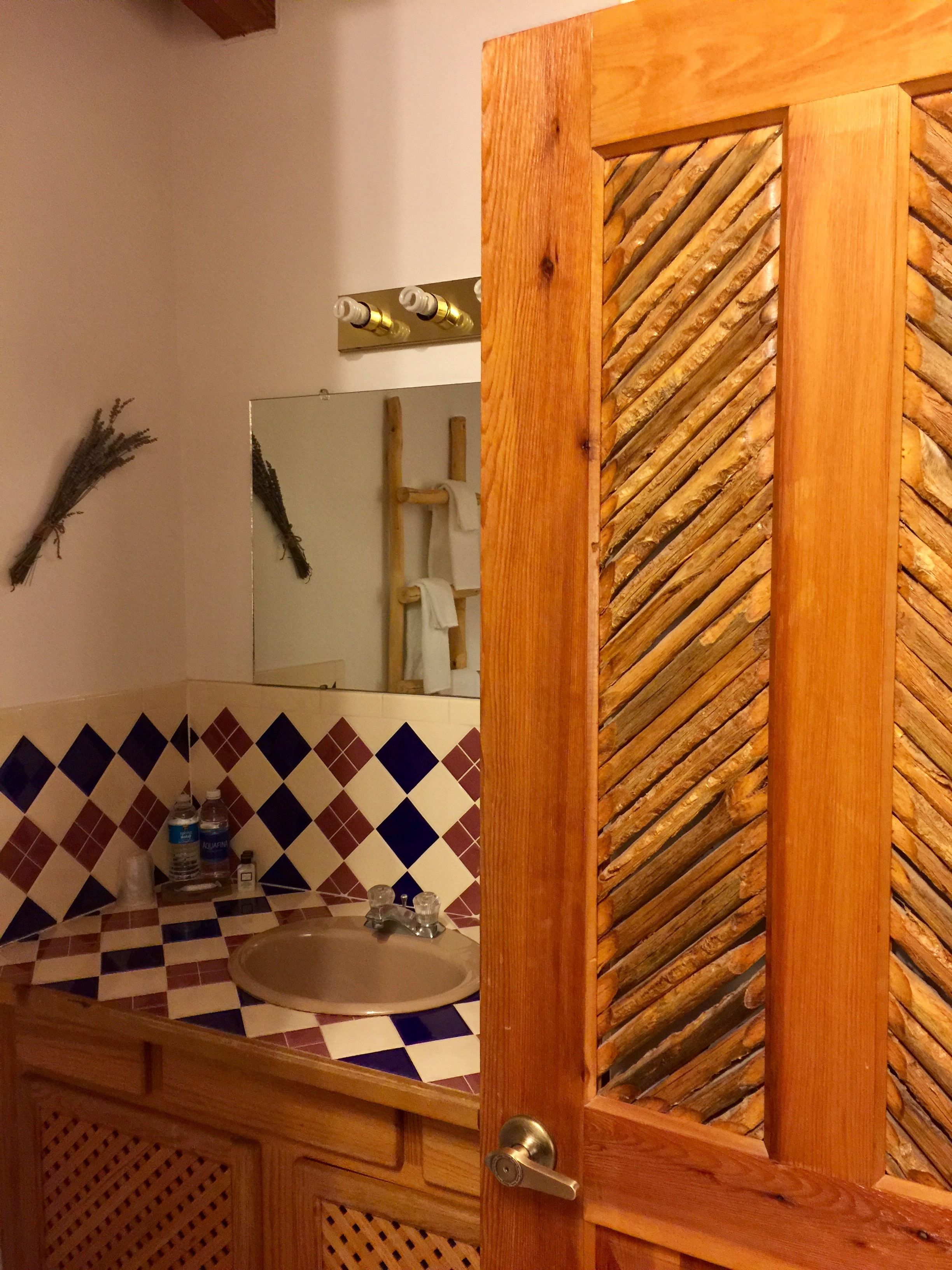 A wooden door with a glass panel, a bathroom sink, a mirror, and a tiled backsplash.