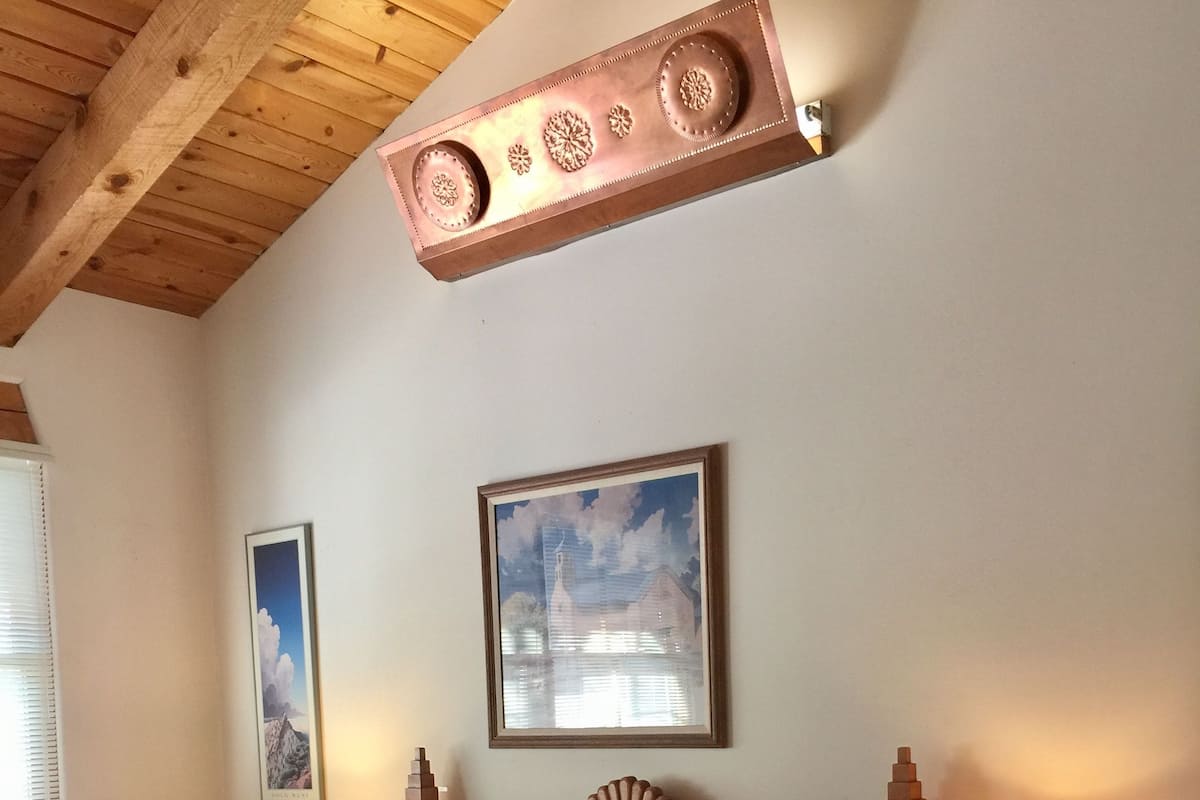 Quarto com cama, duas mesas de cabeceira, abajur, quadro emoldurado na parede e teto de madeira.