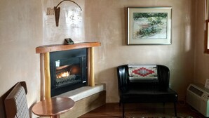 A cozy living room with a fireplace, a framed landscape painting, a black leather chair, and a small table. - Guadalupe Inn (Santa Fe)