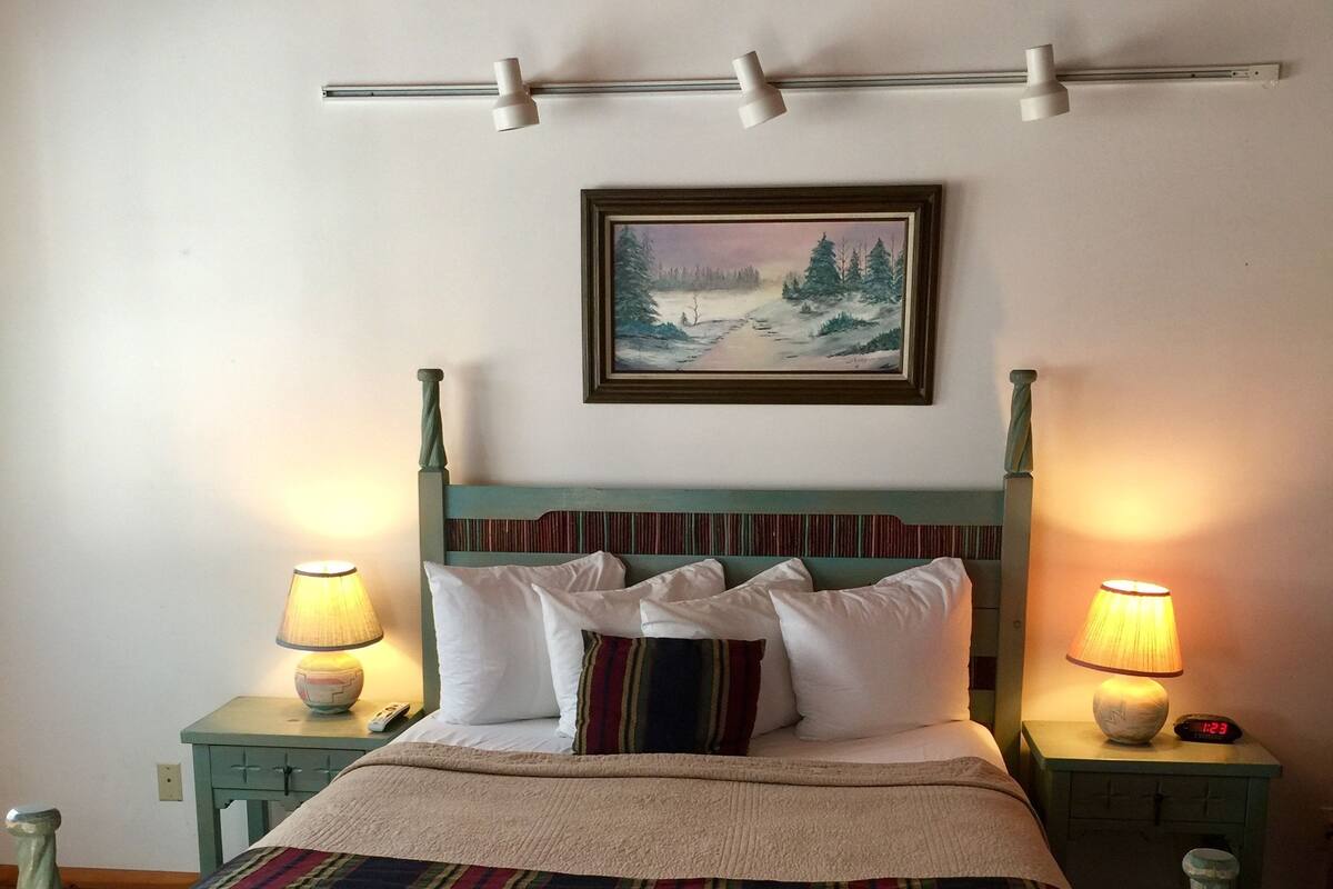 Uma cama com um cobertor listrado, duas luminárias de cabeceira e um quadro na parede.