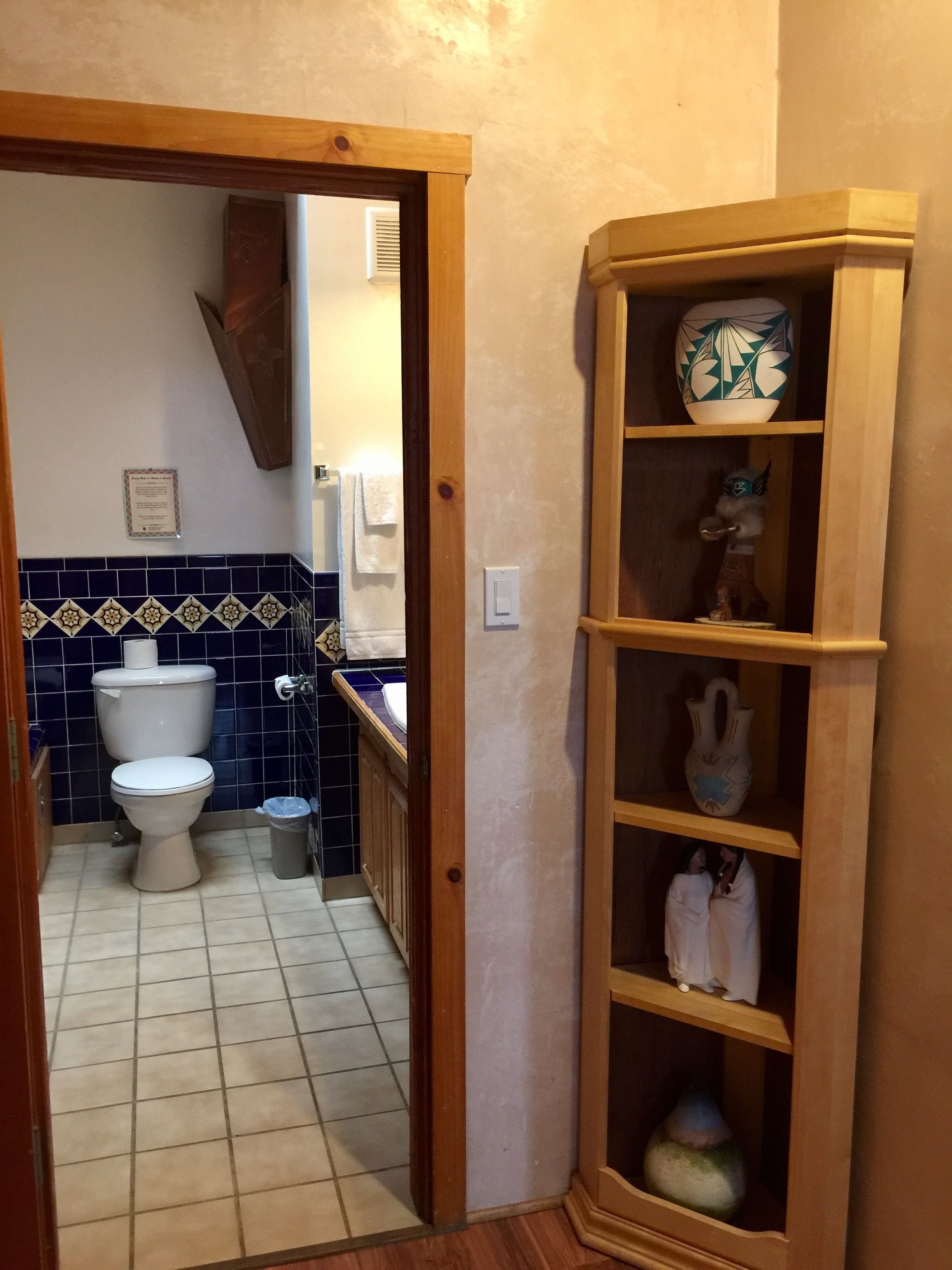 Un pasillo estrecho que da a un baño con inodoro, lavamanos y paredes de azulejos azules.