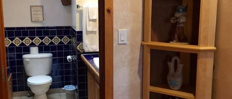 A narrow hallway leading to a bathroom with a toilet, sink, and blue-tiled walls.
