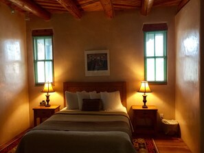 A bedroom with a wooden headboard, two bedside lamps, a bed with multiple pillows, and a framed picture on the wall. - Guadalupe Inn (Santa Fe)