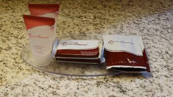 A countertop with a clear glass dish holding three items: a tube of RainBreeze Conditioning Shampoo, a bar of Gentle Cleansing Face & Body Bar, and a tube of RainBreeze Body Lotion.