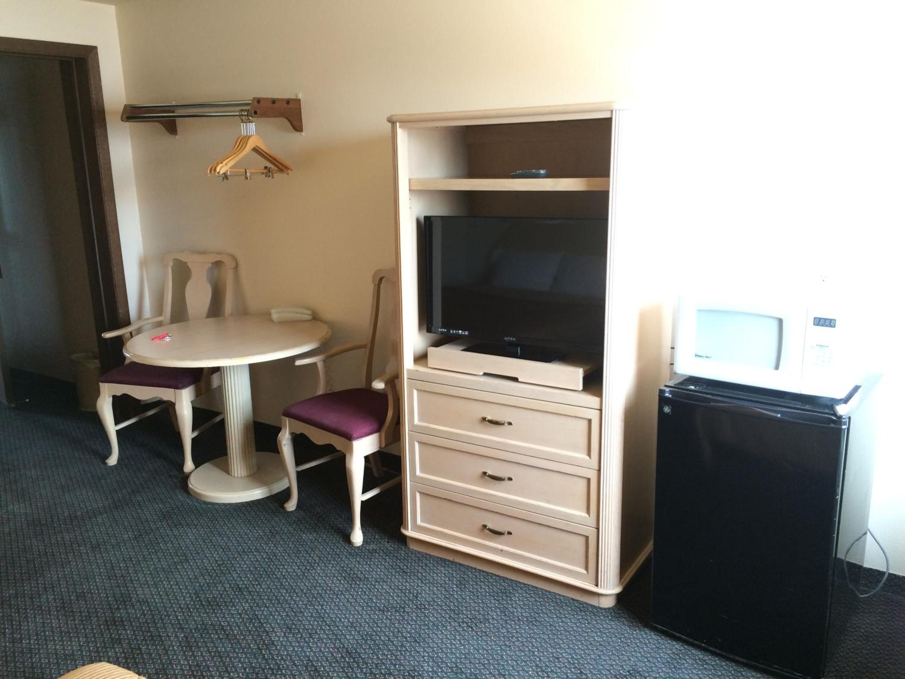 A compact hotel room with a small round table, two chairs, a television, a minibar, and a coat rack.