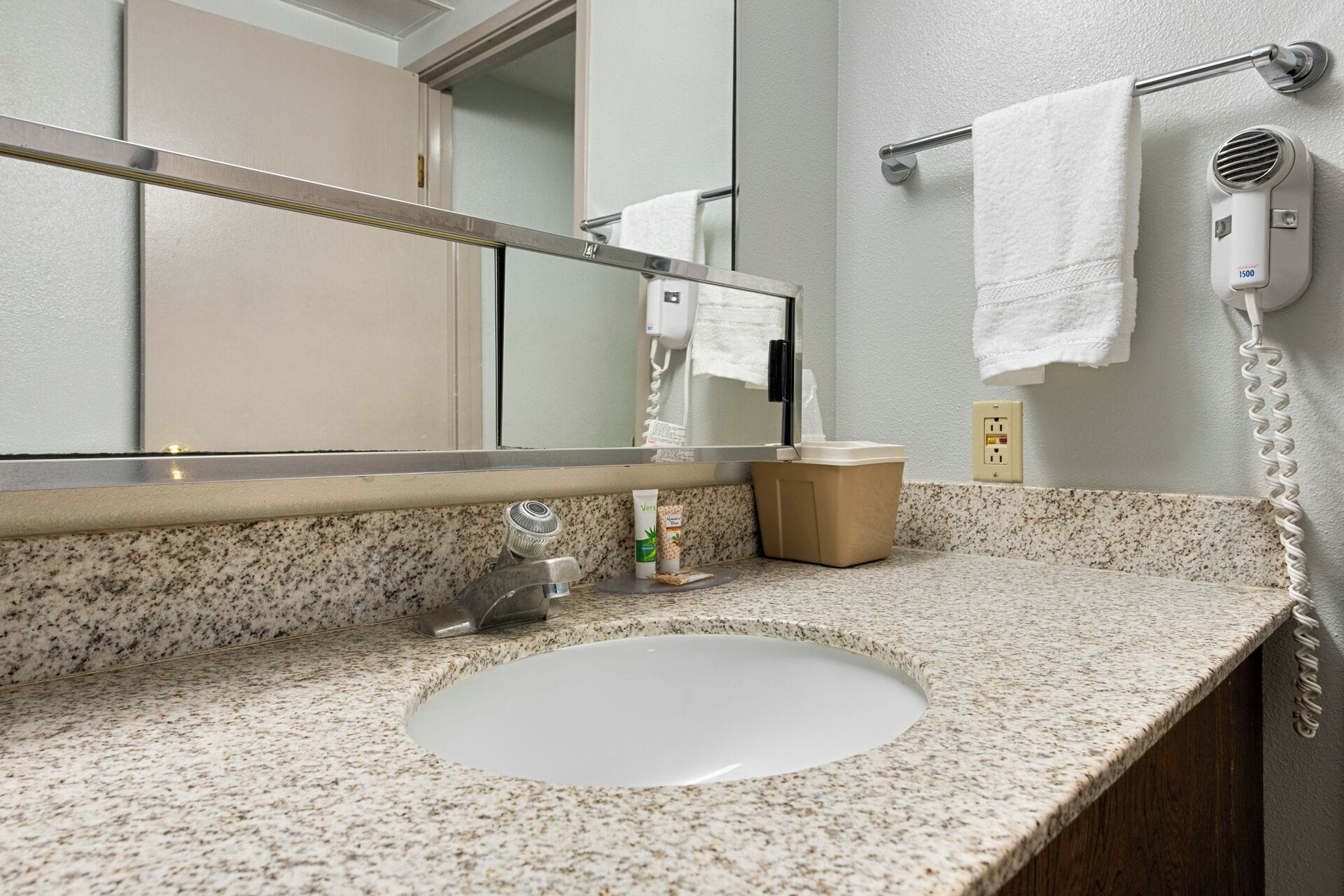 A bathroom with a granite countertop, a sink, a mirror, a towel rack, and a hair dryer.