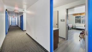 Pasillo de hotel con puertas azules, alfombra estampada y un baño visible con ventana.